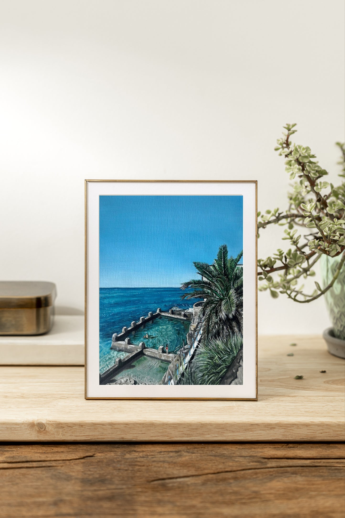 An original oil painting depicting Coogee Beach and Ocean Pool with a clear blue sky, palm trees, and people in the background. One of the most iconic beaches in Sydney.